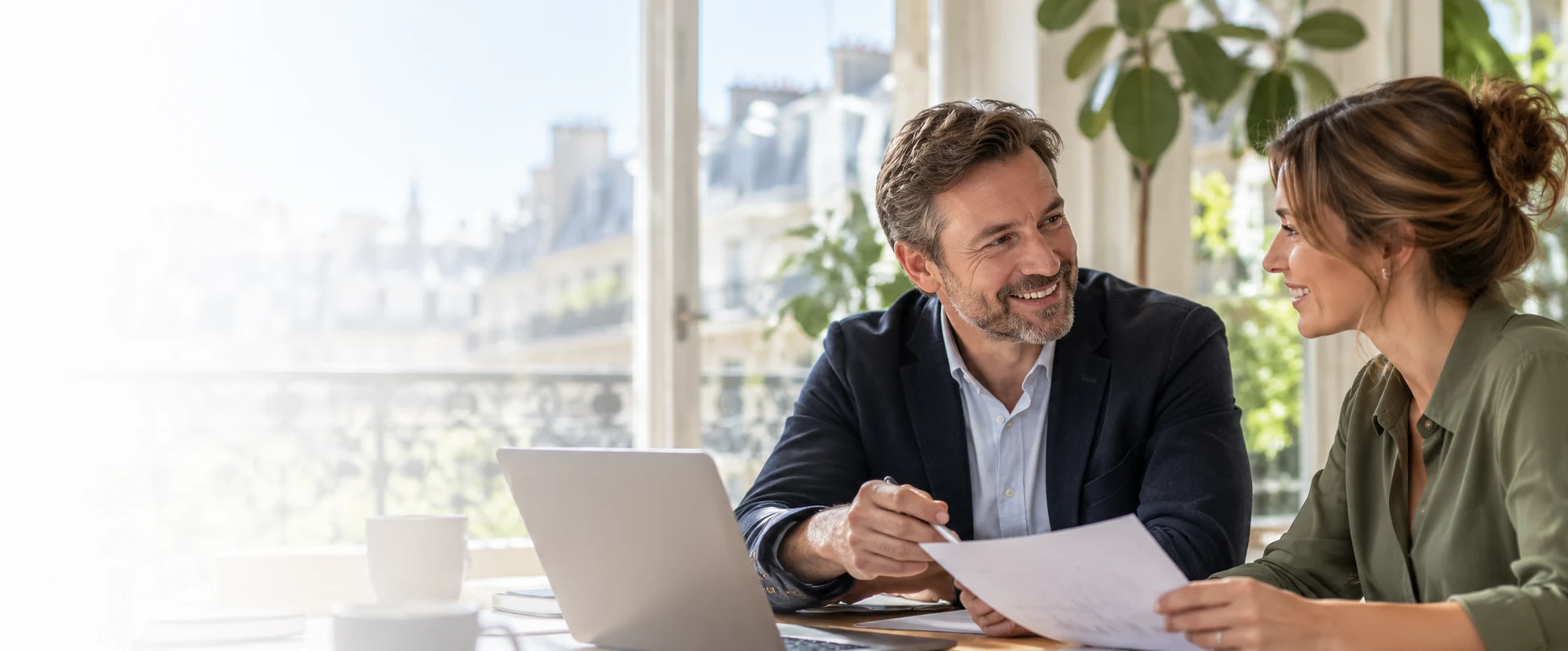 Deux professionnels en échange autour d'un ordinateur portable dans un bureau lumineux, illustrant la relation client développée avec MADCRM